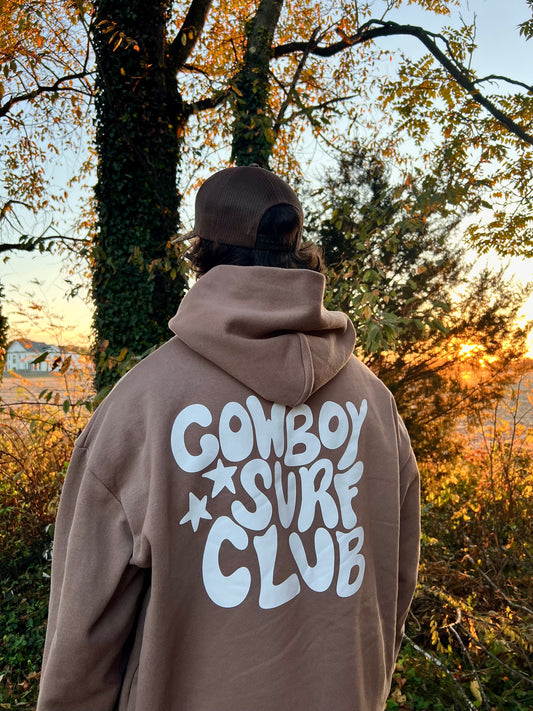 Person wearing a hoodie with 'Cowboy Surf Club' text in an outdoor setting