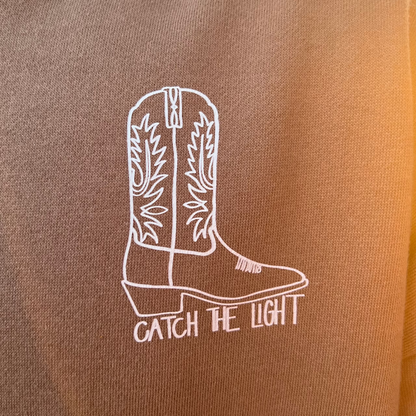 Brown hoodie with a white cowboy boot design and text on the back.