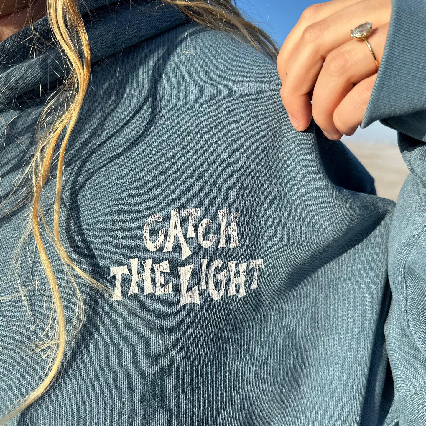 Person wearing a hoodie with 'Catch The Light' text on the back, outdoors.
